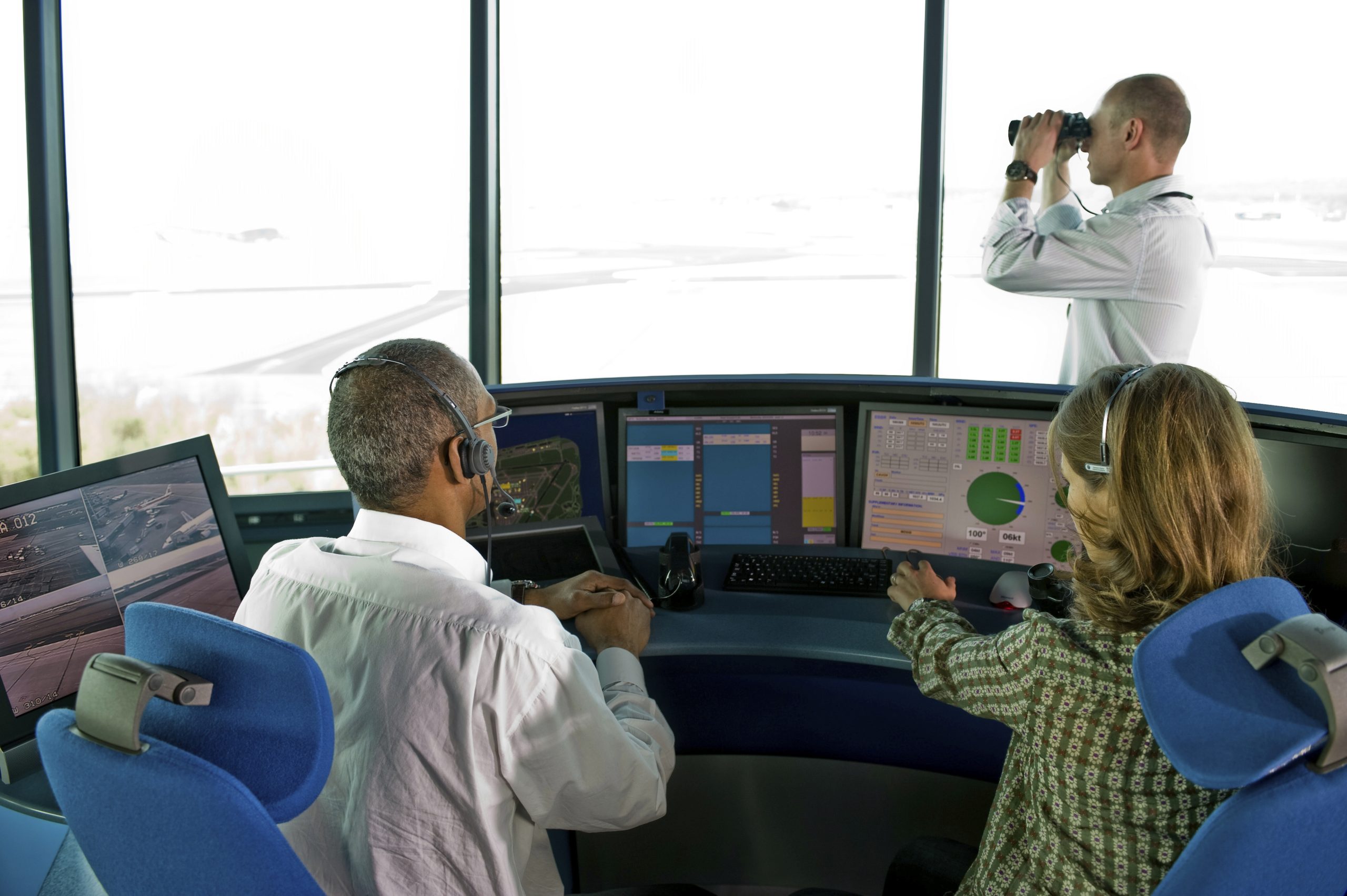 people working airport control tower EVCS system and primary VCCS operations in an air traffic control tower, with controllers monitoring communication systems and airport activity.